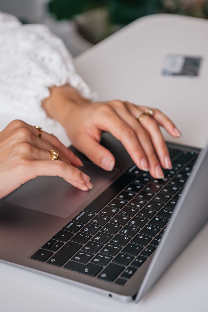 ours-journey Hands of a woman typing on a laptop keyboard indoors, showcasing rings and fashion.